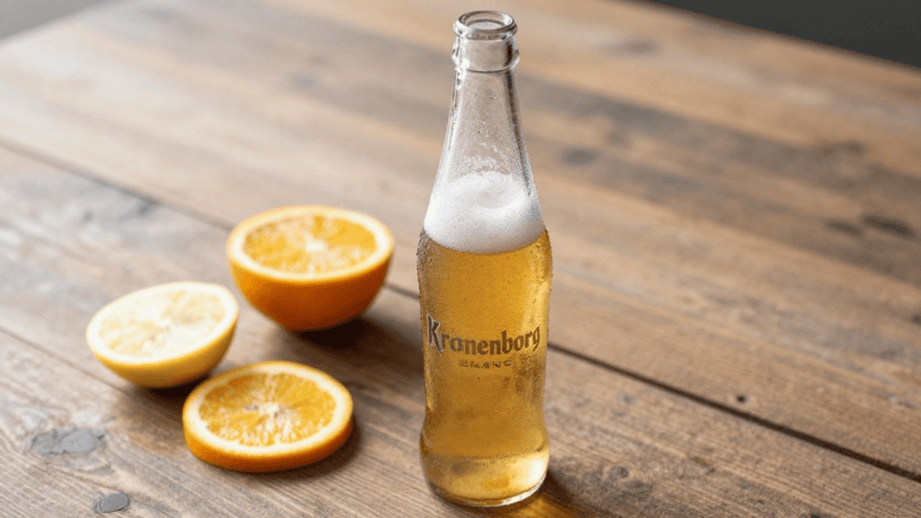 Kronenborg beer bottle with condensation on a wooden table, beside orange and lemon halves.