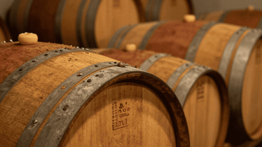 Row of oak wine barrels in a dimly lit cellar, metal hoops visible along the staves.