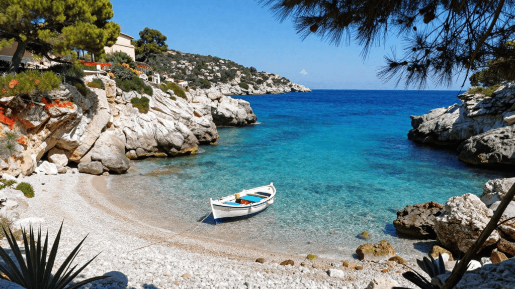 Small white boat resting on a pebbly beach in a turquoise cove formed by rocky cliffs and trees nearby