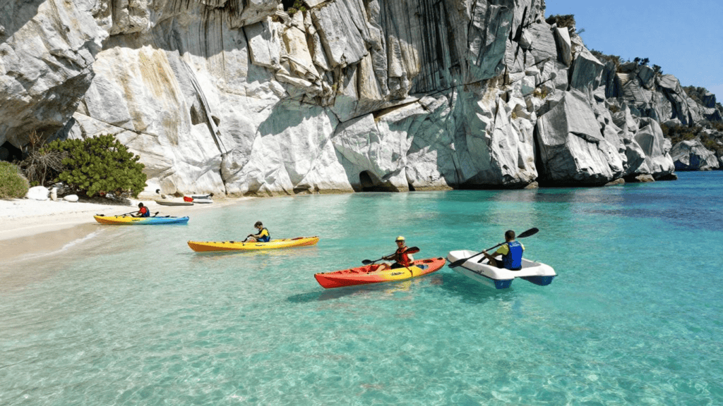 Group of people kayaking near a white rocky cliff on a clear turquoise bay with pale sand beach.