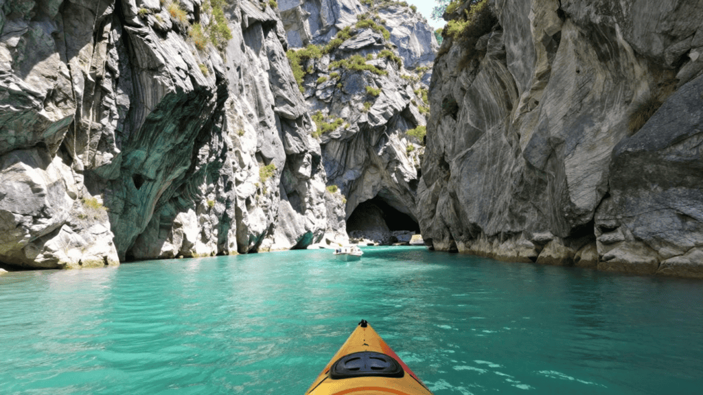 Kayak gliding through a turquoise canyon with steep gray rock walls and a distant cave entrance ahead.