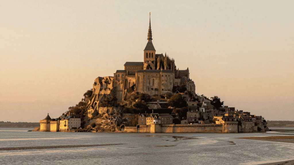 Mont Saint-Michel, a medieval monastery atop a rocky island with surrounding village walls, bathed in golden sunset light.