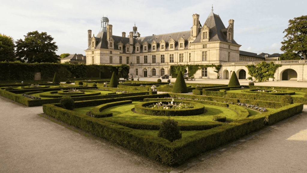 Grand stately château with ornate stonework and a formal parterre garden in front.